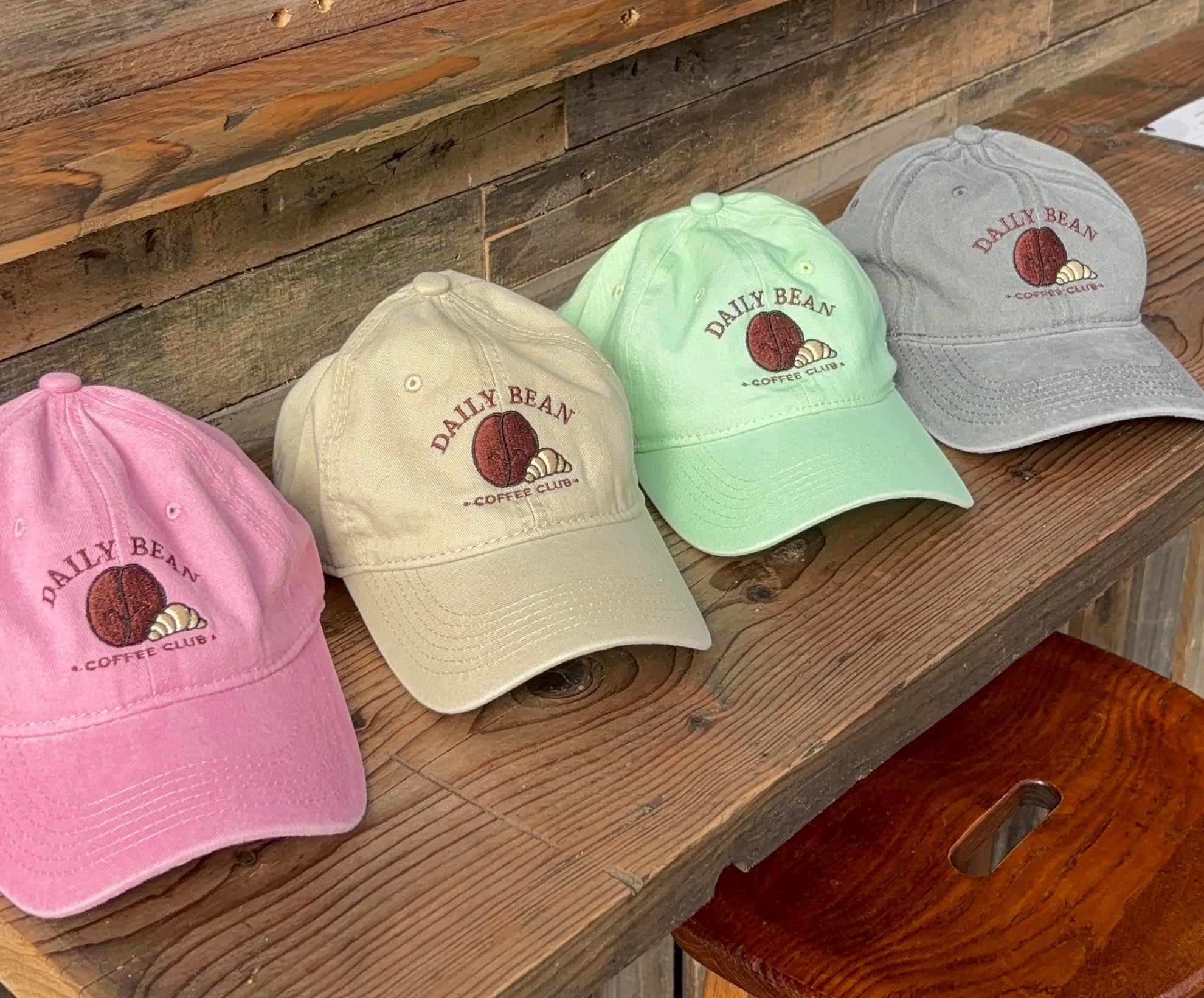 Four baseball caps in different colors on a wooden surface with a chalkboard in the background.