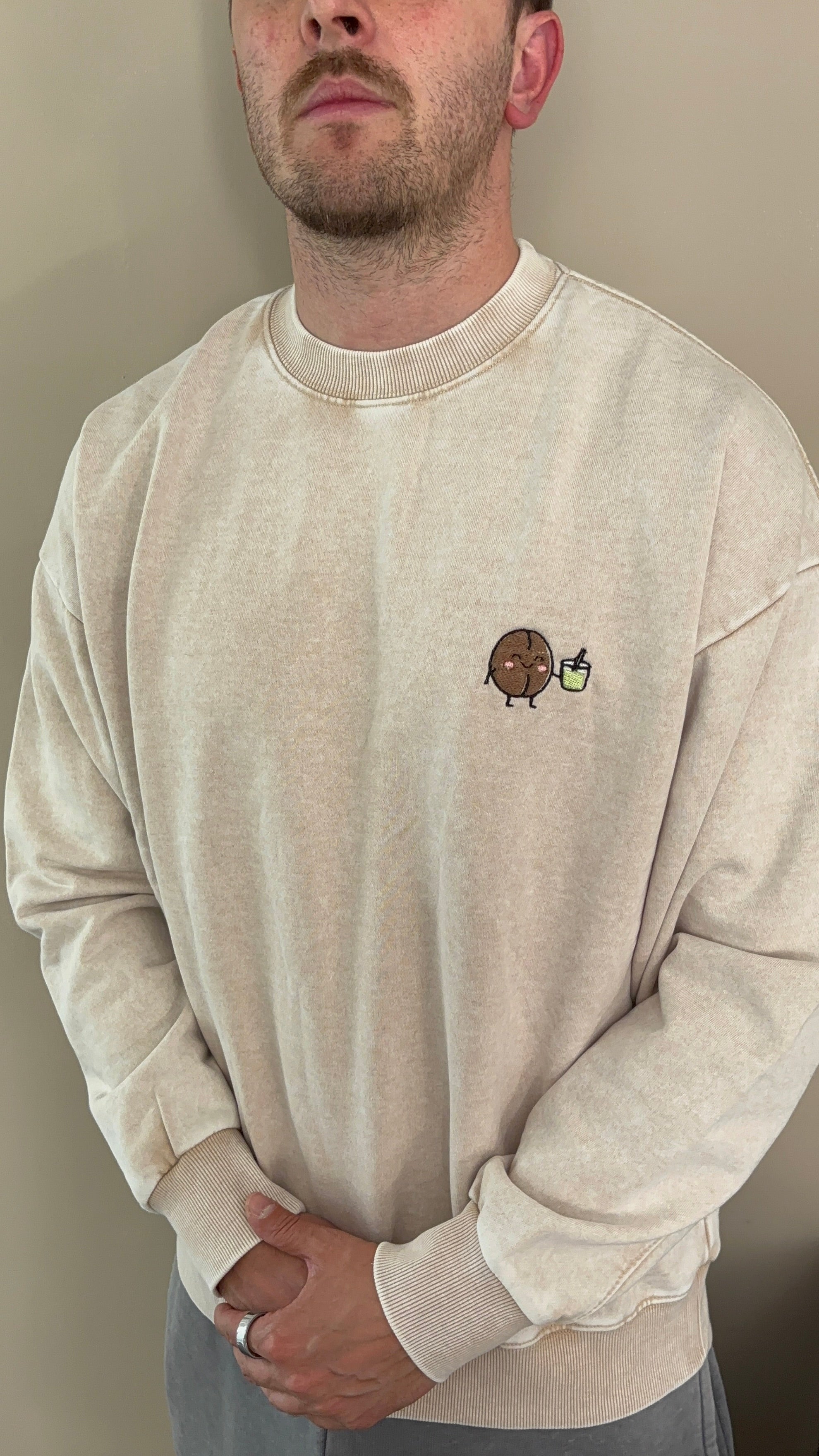 Person wearing a beige sweatshirt with a small graphic on a plain background