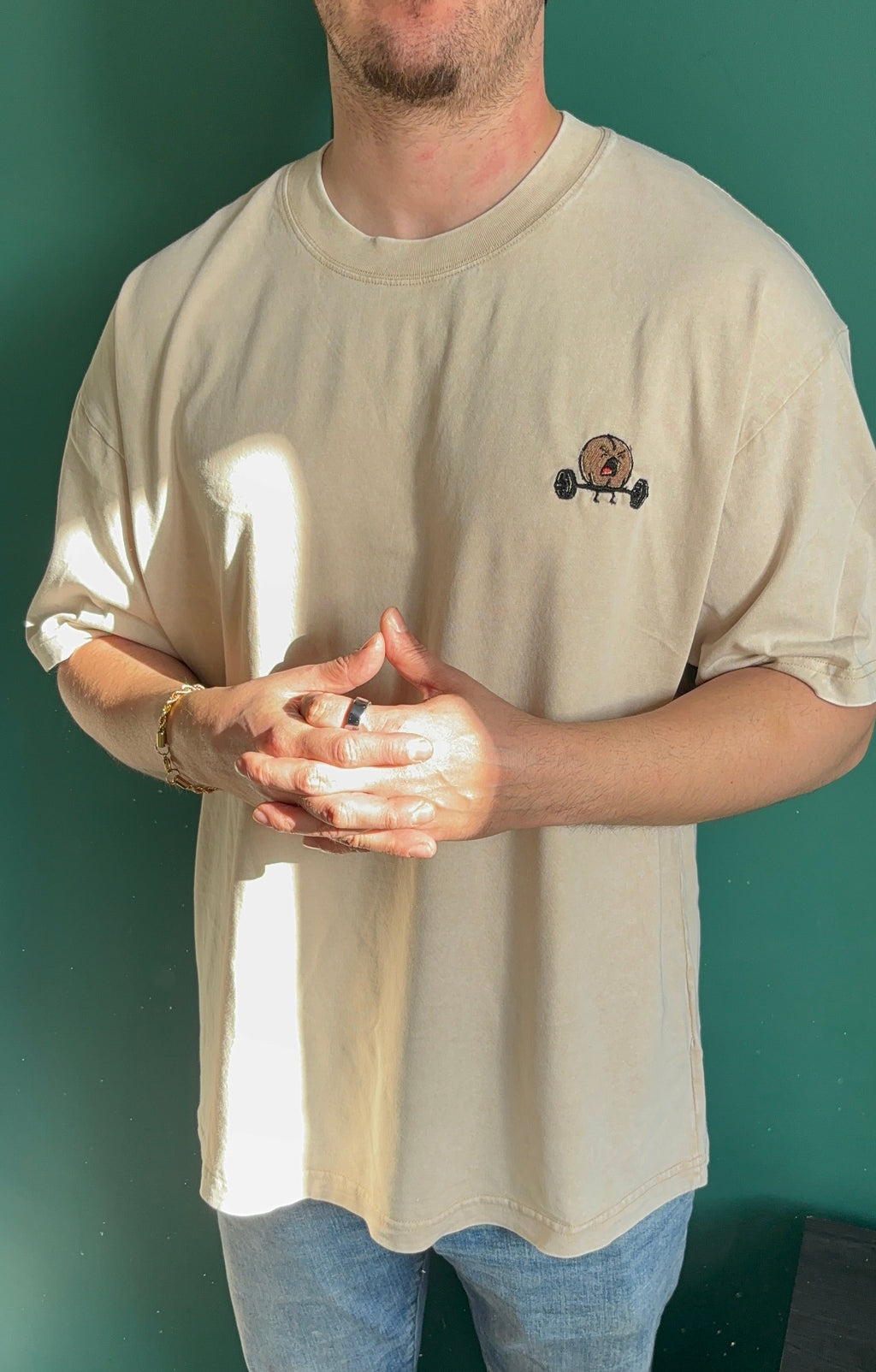 Man wearing a beige t-shirt with a small graphic on a green wall