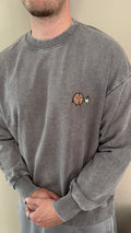 Person wearing a gray sweatshirt with a small embroidered design on the chest.