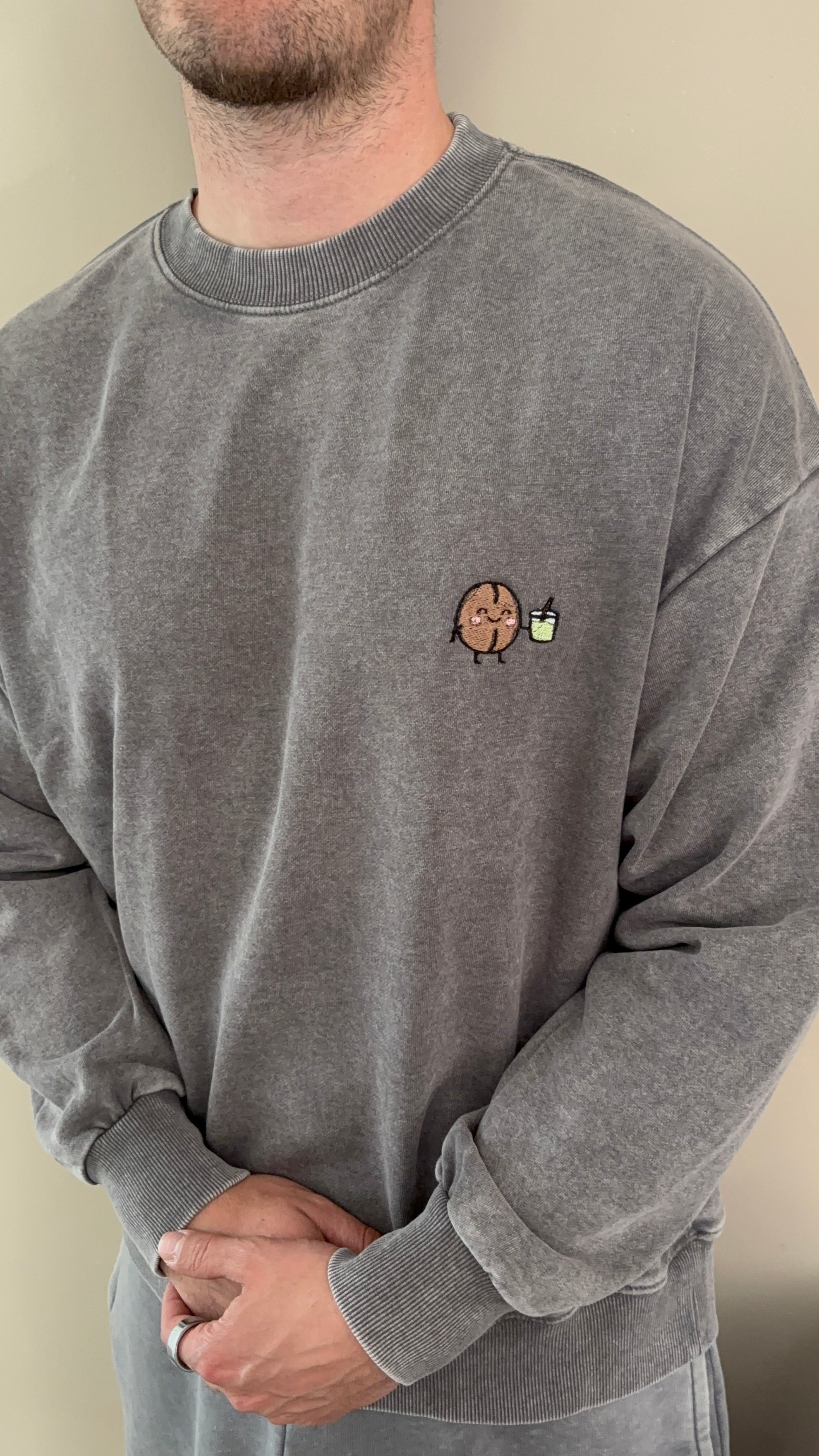 Person wearing a gray sweatshirt with a small embroidered design on the chest.
