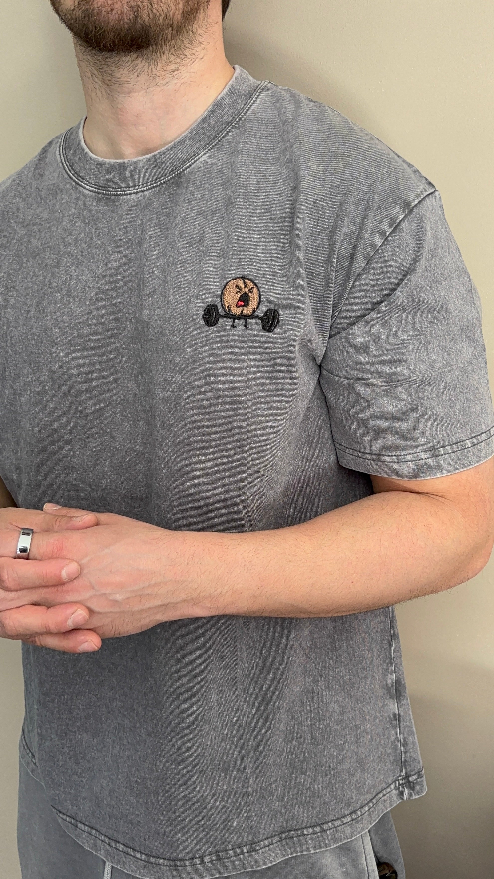 Person wearing a gray t-shirt with a small graphic on a plain background