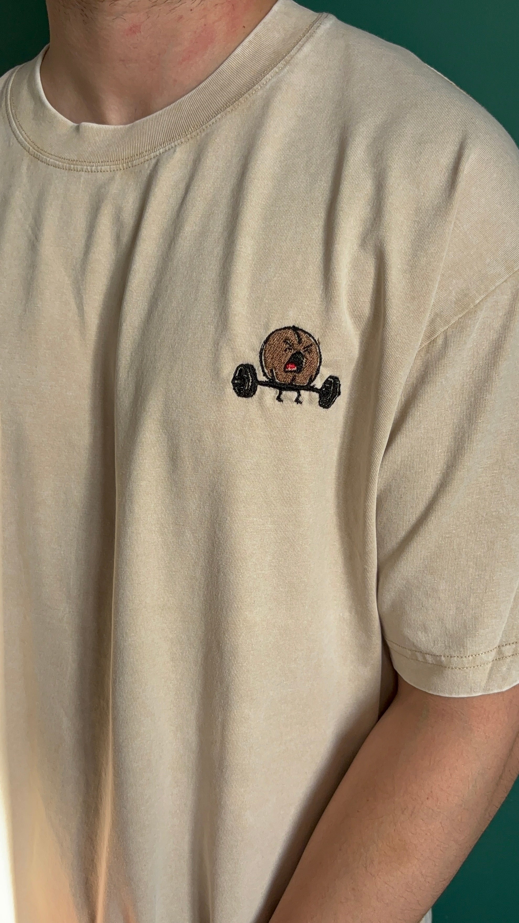 Beige t-shirt with a small graphic of a bear lifting weights on the chest.