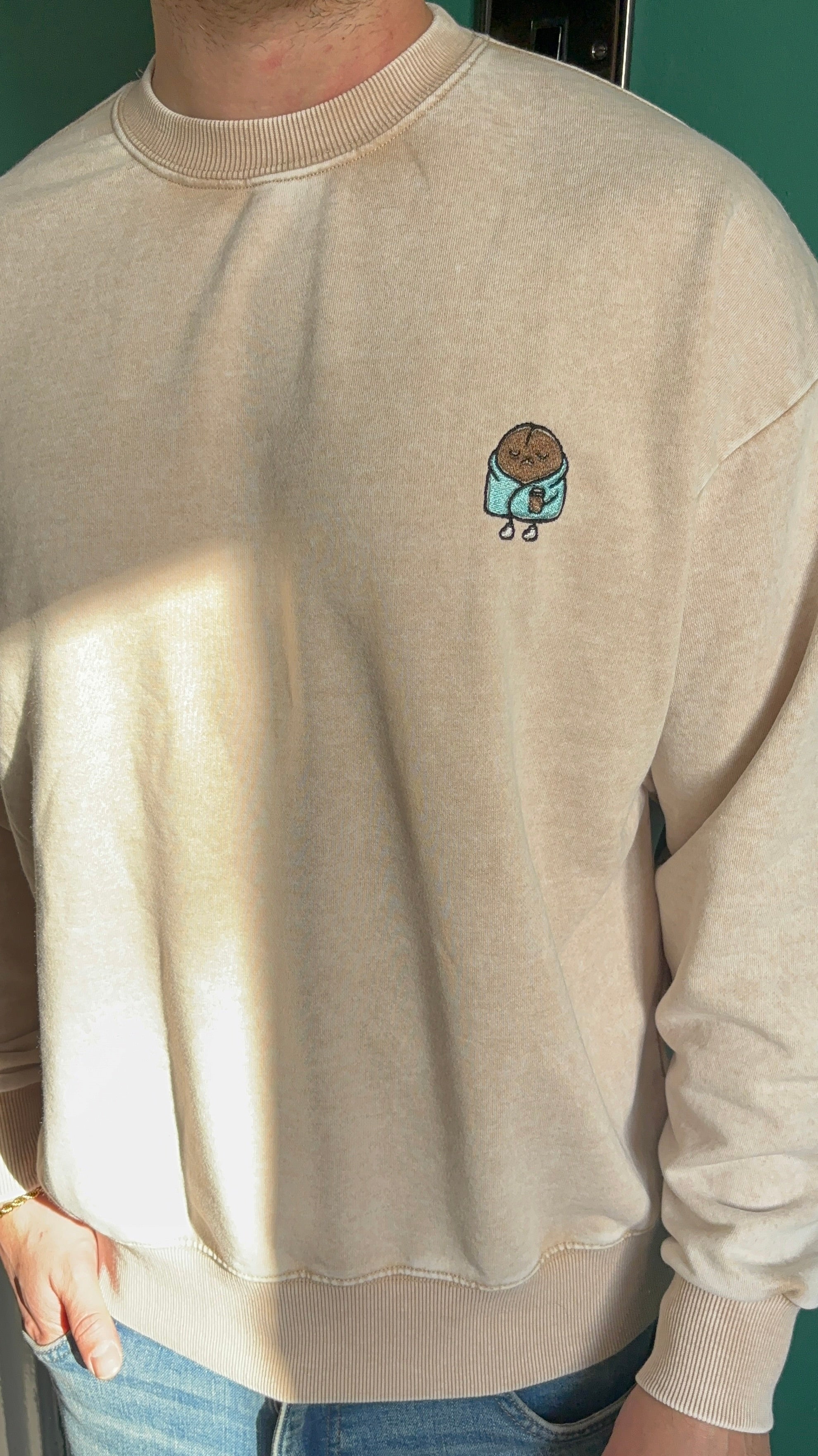 Beige sweatshirt with a small embroidered design on the chest.