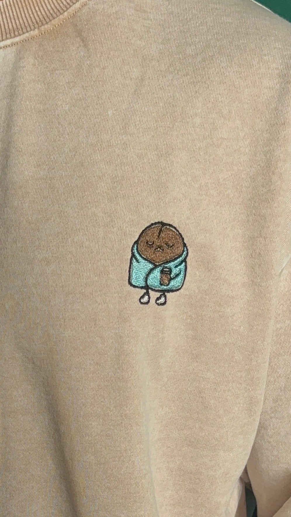 Beige sweatshirt with a small embroidered design on the chest.