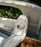 An off-white baseball cap with a brown embroidered logo reading 'DAY BEAN' and 'SANTA MONICA' resting on the back of a car seat inside a vehicle.