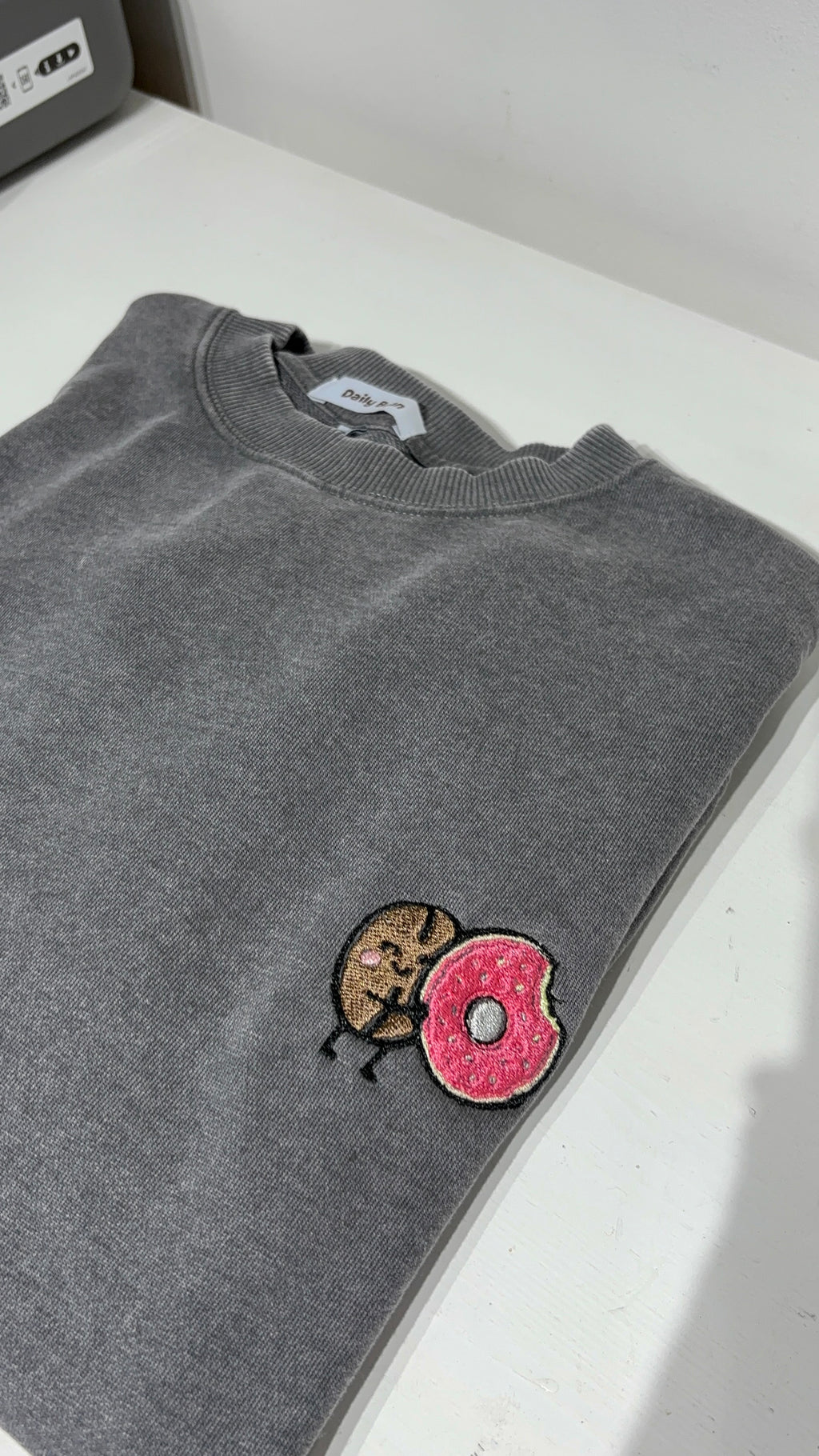 Gray sweatshirt with a cartoon character and pink donut patch on a white surface