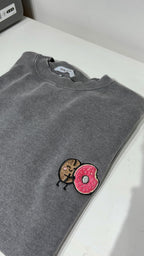 Gray sweatshirt with a cartoon character and pink donut patch on a white surface