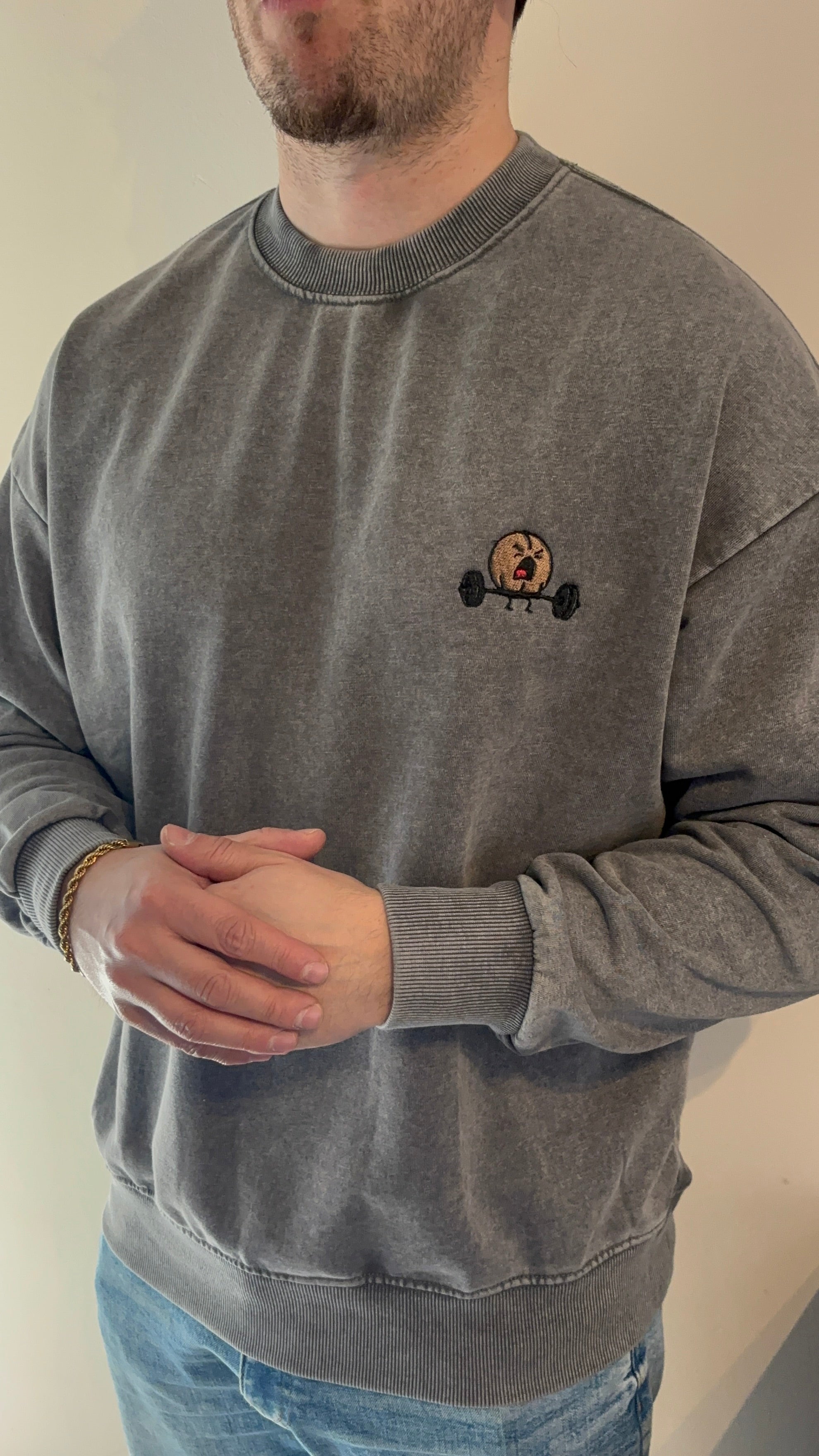 Person wearing a gray sweatshirt with a small logo on a plain background