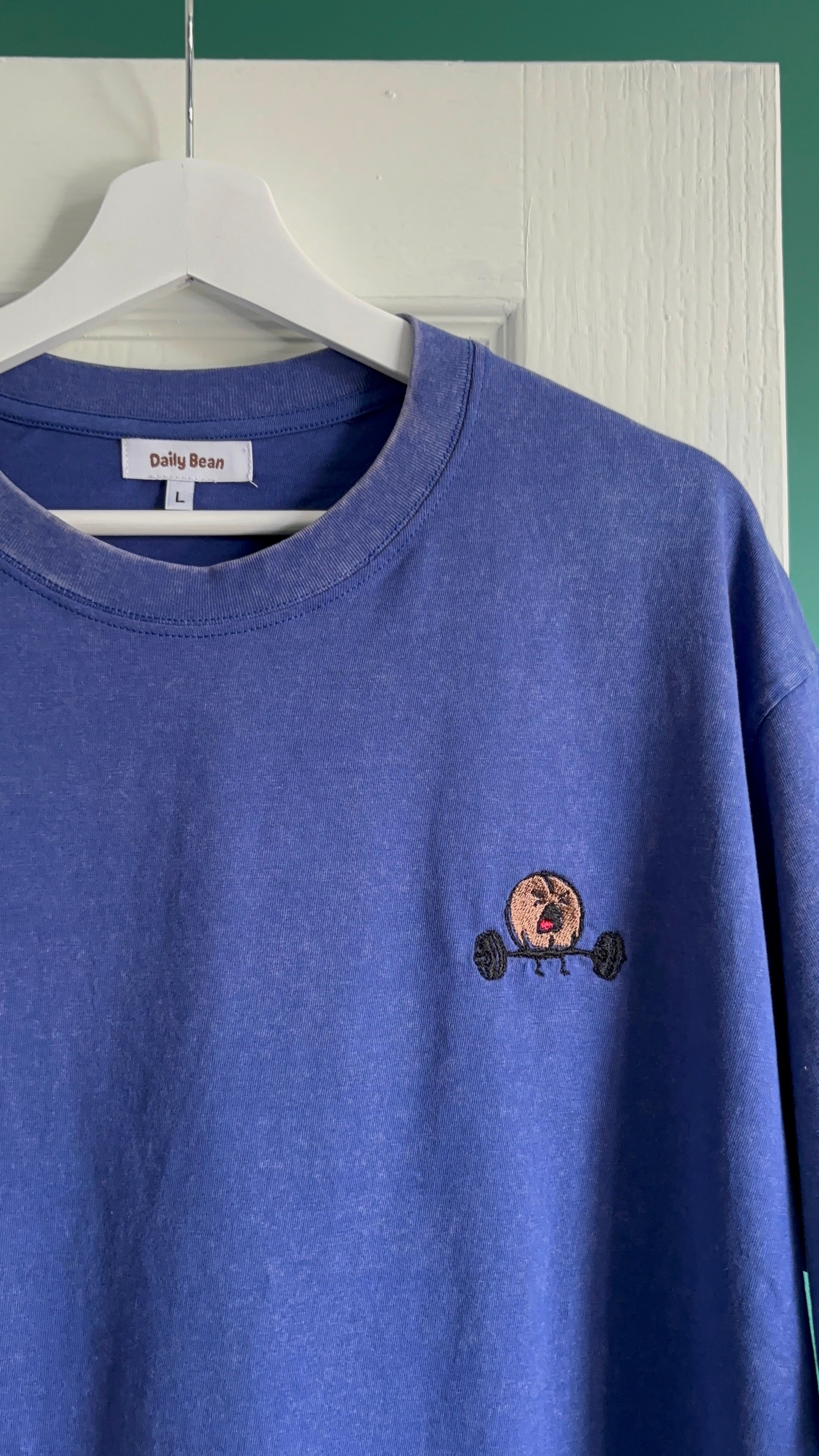 Blue sweatshirt with a small embroidered design on a hanger against a white wall.