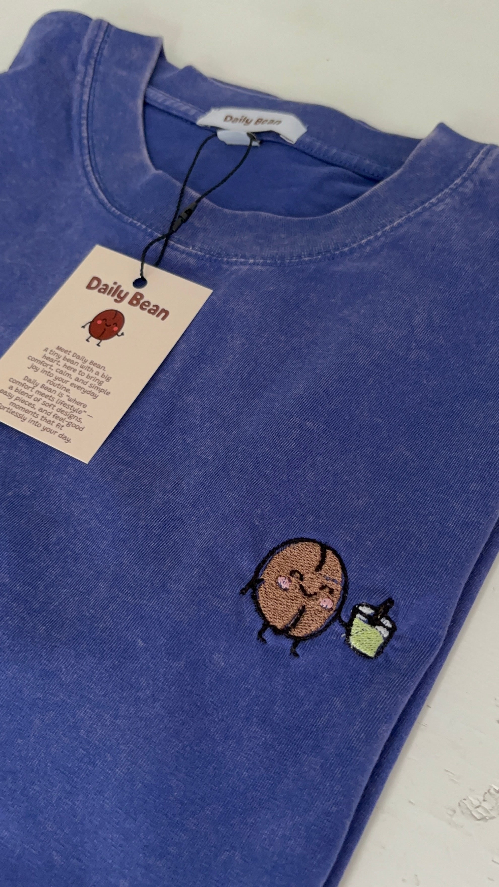 Blue sweatshirt with an embroidered design and a tag on a white background