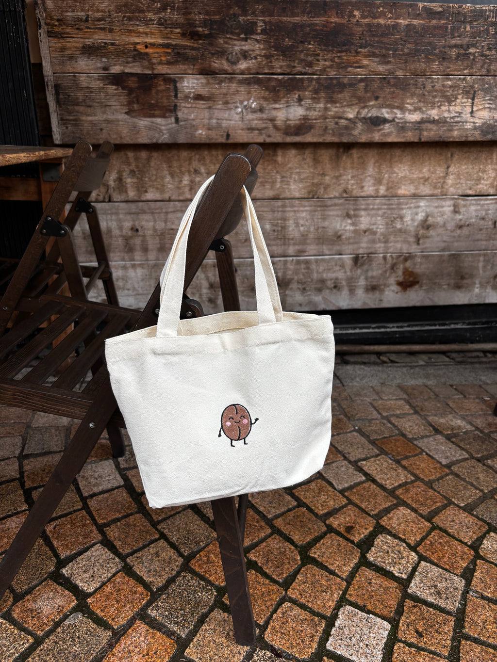 White tote bag with a small design on a wooden chair outdoors.