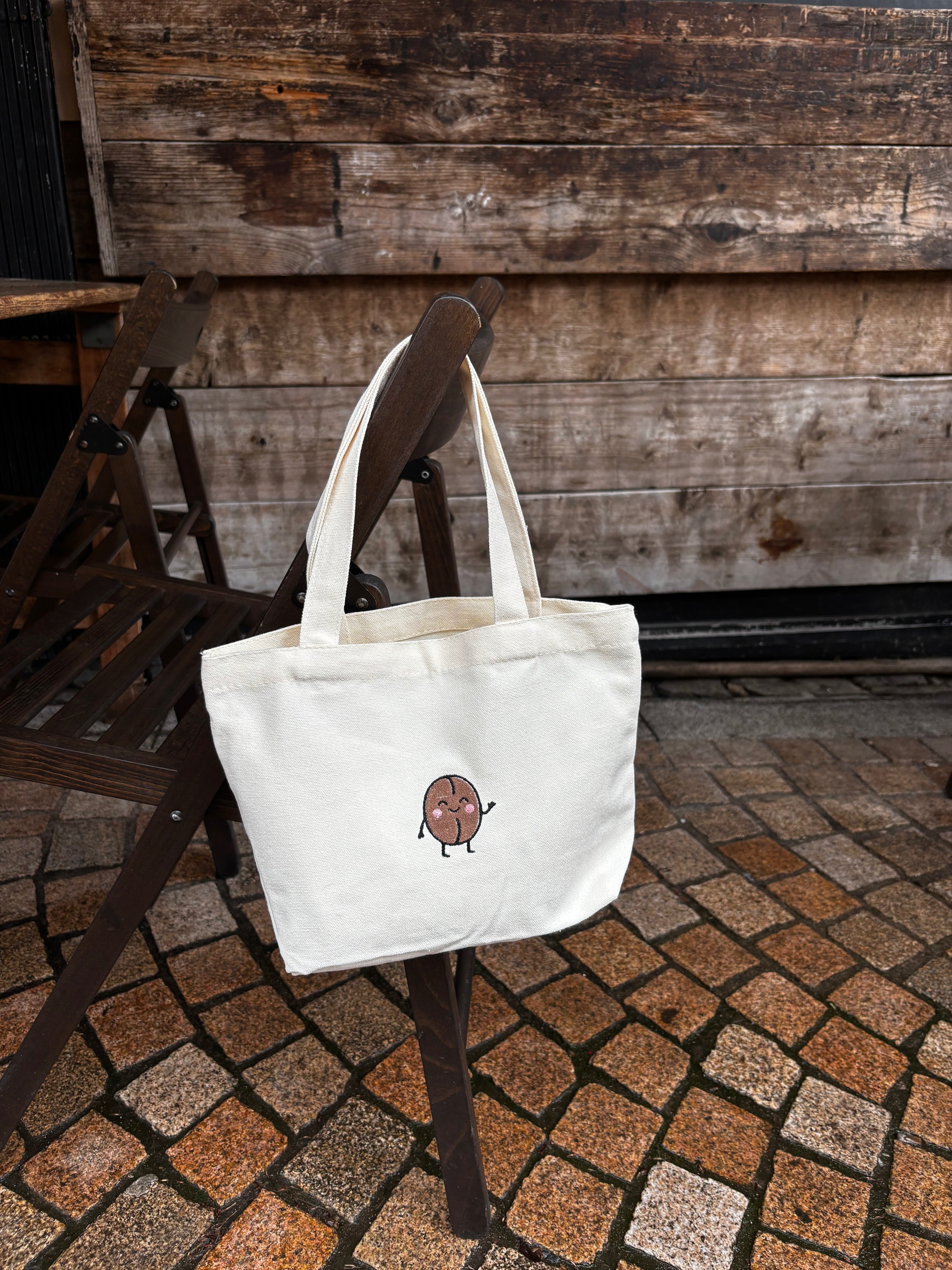White tote bag with a small design on a wooden chair outdoors.