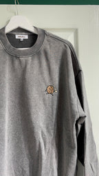 Gray sweatshirt with a small logo on a hanger against a white wall.