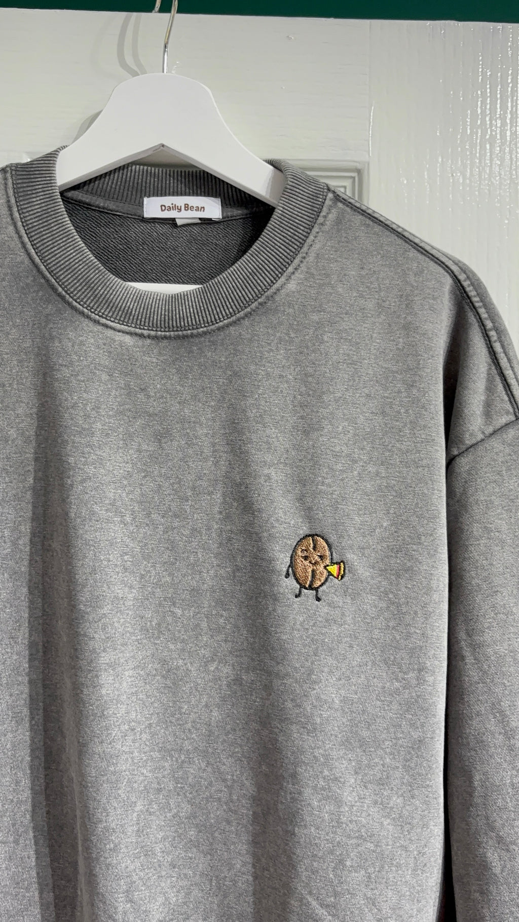Gray sweatshirt with a small embroidered design on a hanger against a white wall.