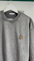 Gray sweatshirt with a small embroidered design on a hanger against a white wall.