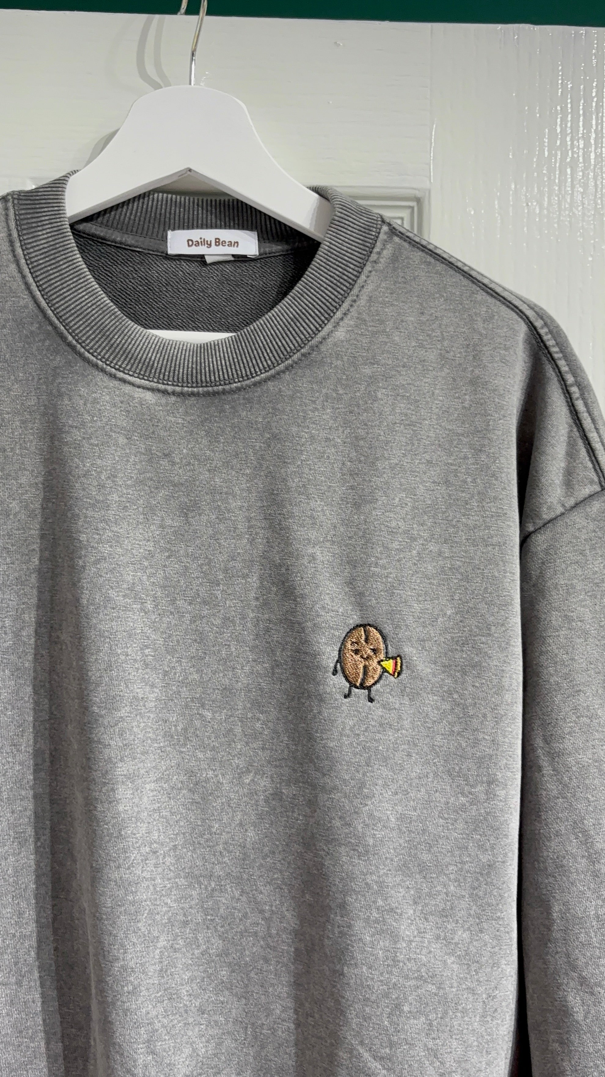 Gray sweatshirt with a small embroidered design on a hanger against a white wall.