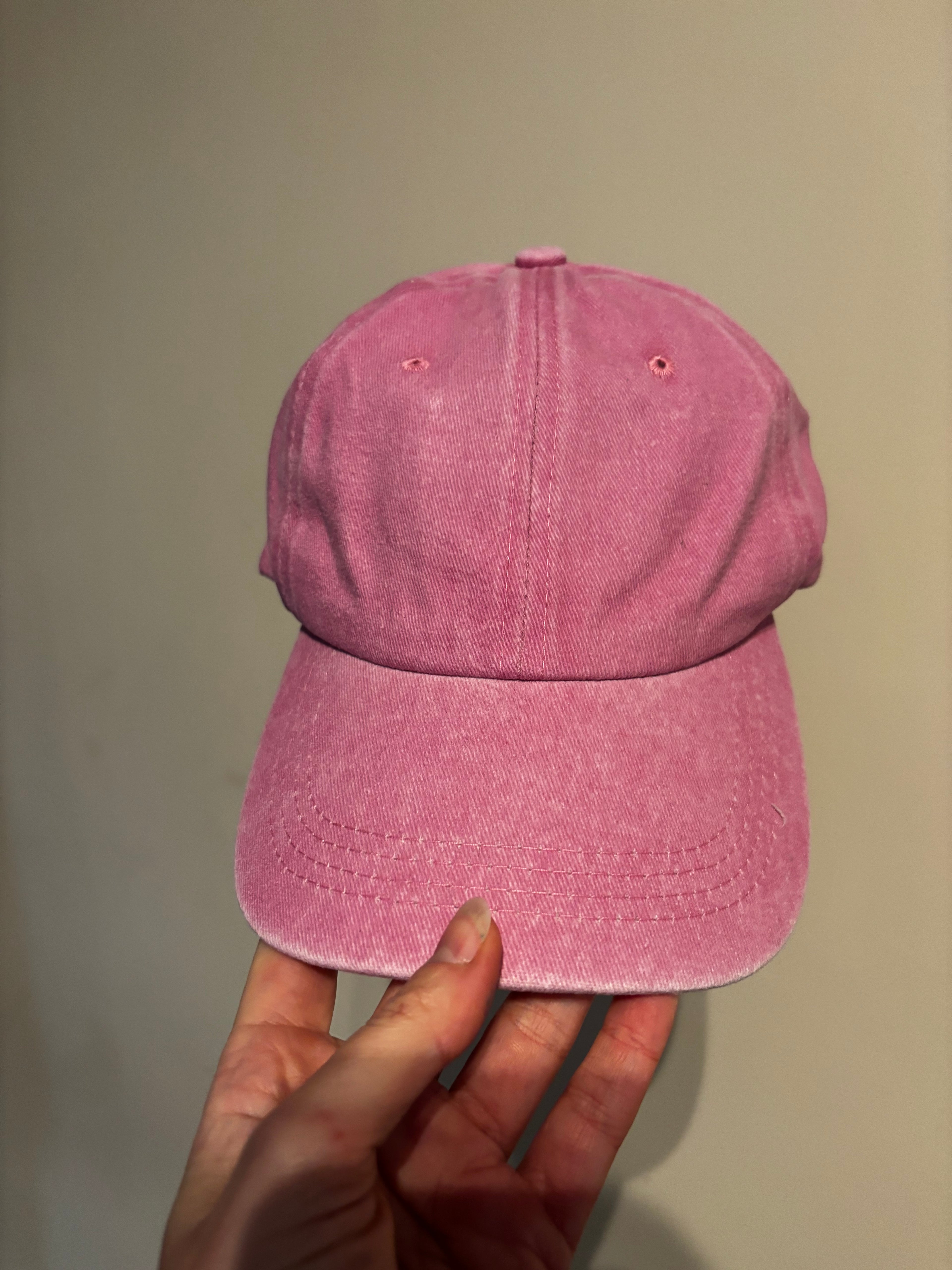 Pink cap held by a hand against a plain background