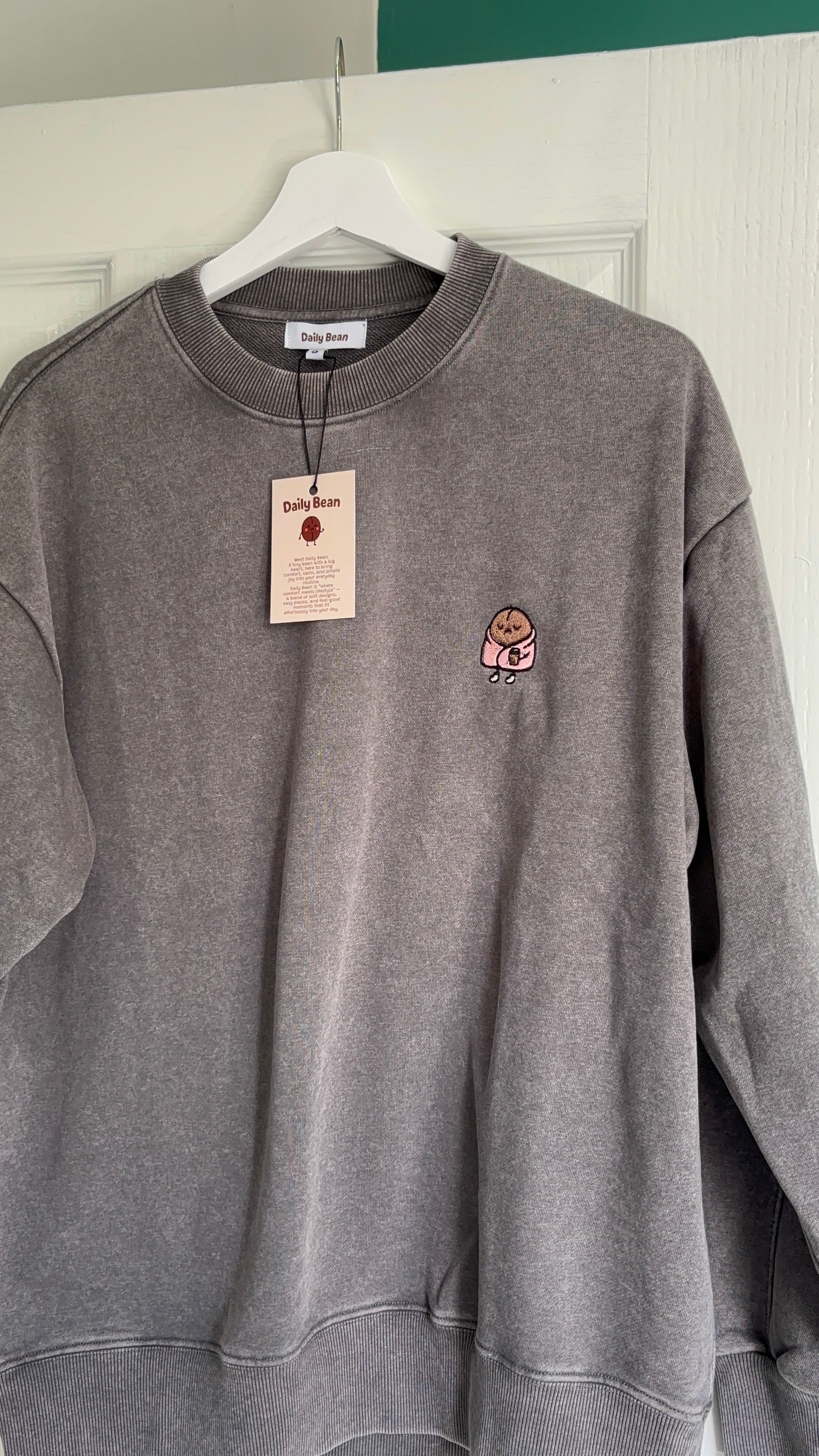 Gray sweatshirt with a small logo on a hanger against a white wall.