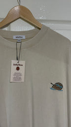 Beige t-shirt with a small logo on a hanger against a white wall.